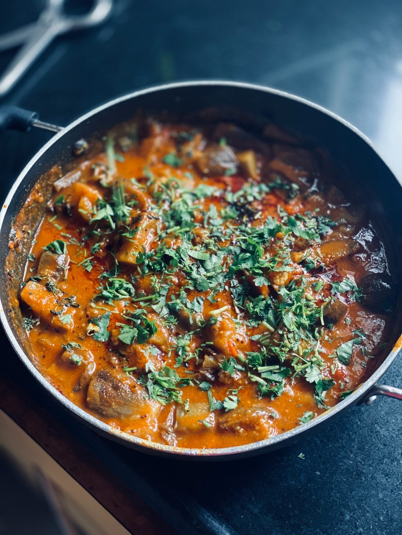 Vegetable curry in a large cooking pan with fresh green herbs